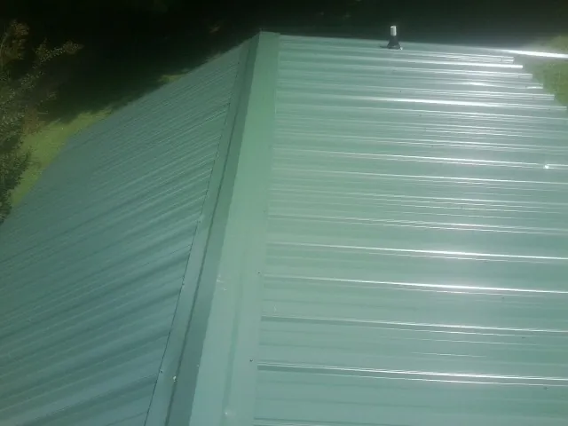 New green metal panels meeting at the ridge of a roof — Flat Roof Repair work by our crew in Exeter