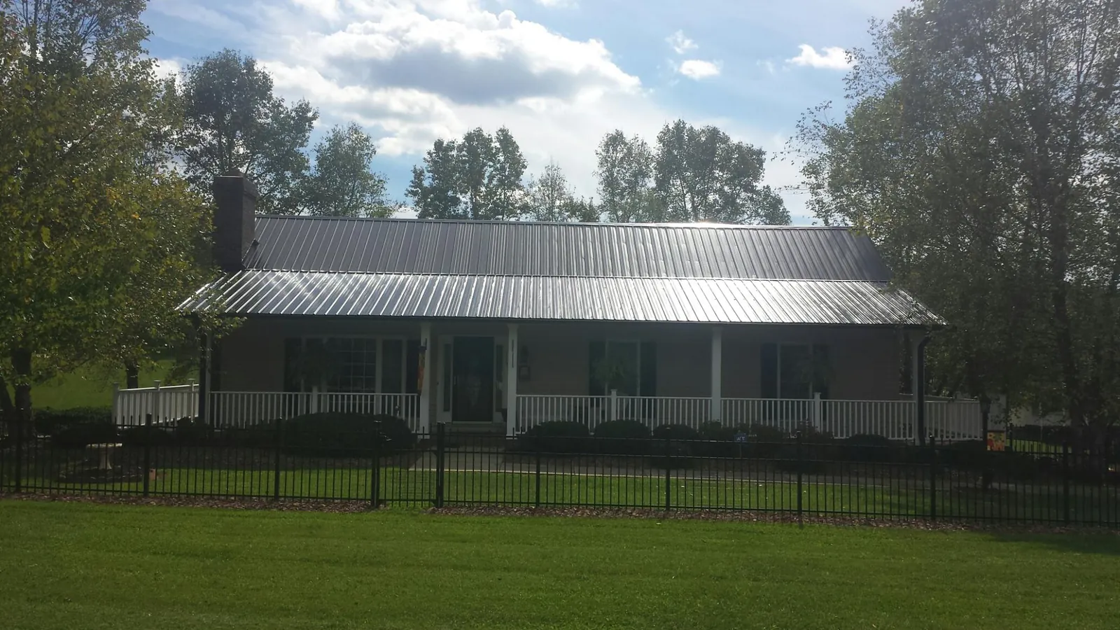 Gray metal roof on a brick ranch with a full width front porch — Gutter Guard Installation work by our crew in Exeter