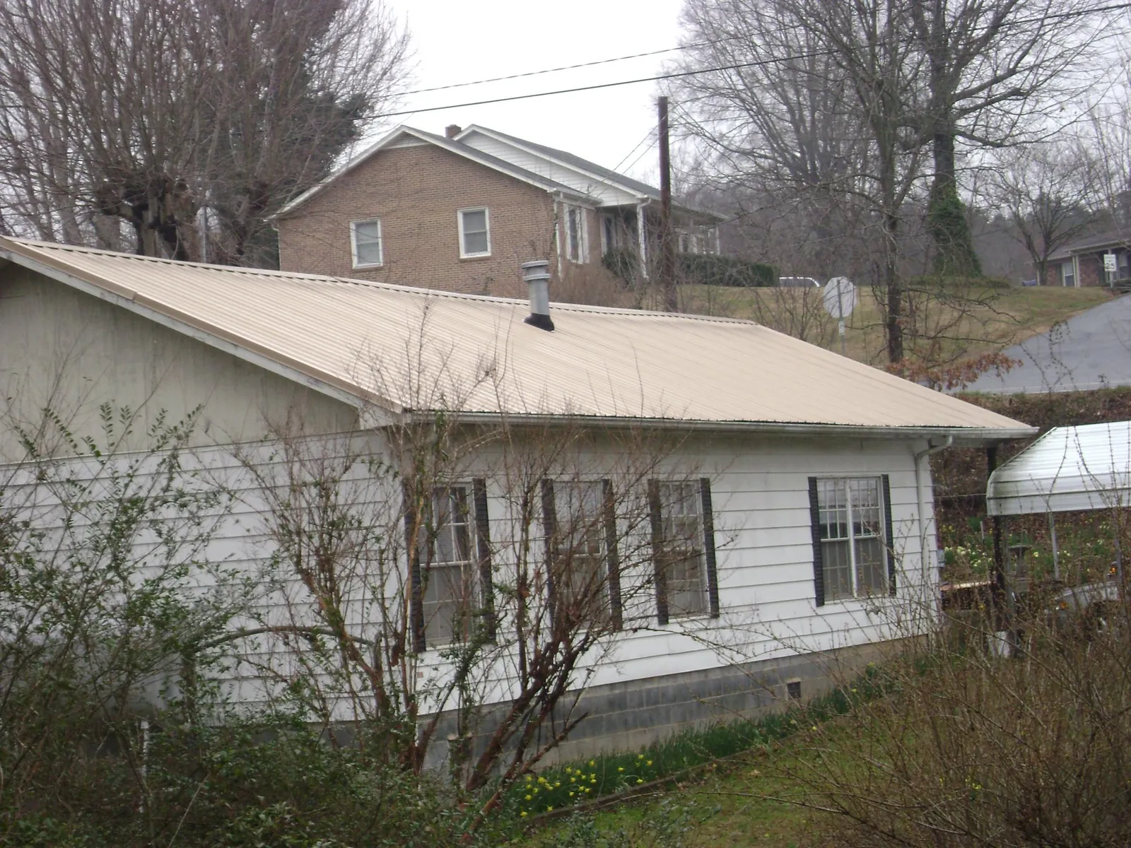 Tan metal roof on a white sided house set into a hillside — Commercial Roofing by Roofing Brothers in Exeter